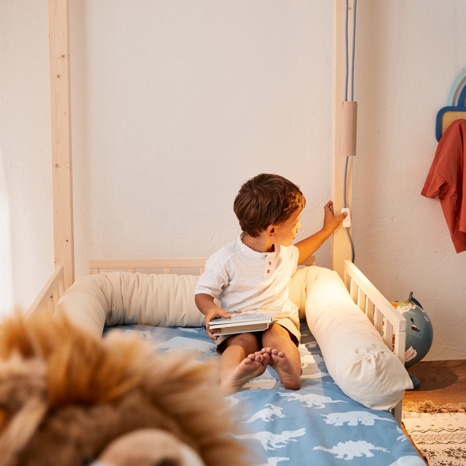 bimbo seduto sul lettino montessori nabè accende luce con paralume cilindrico in legno e filo tessile