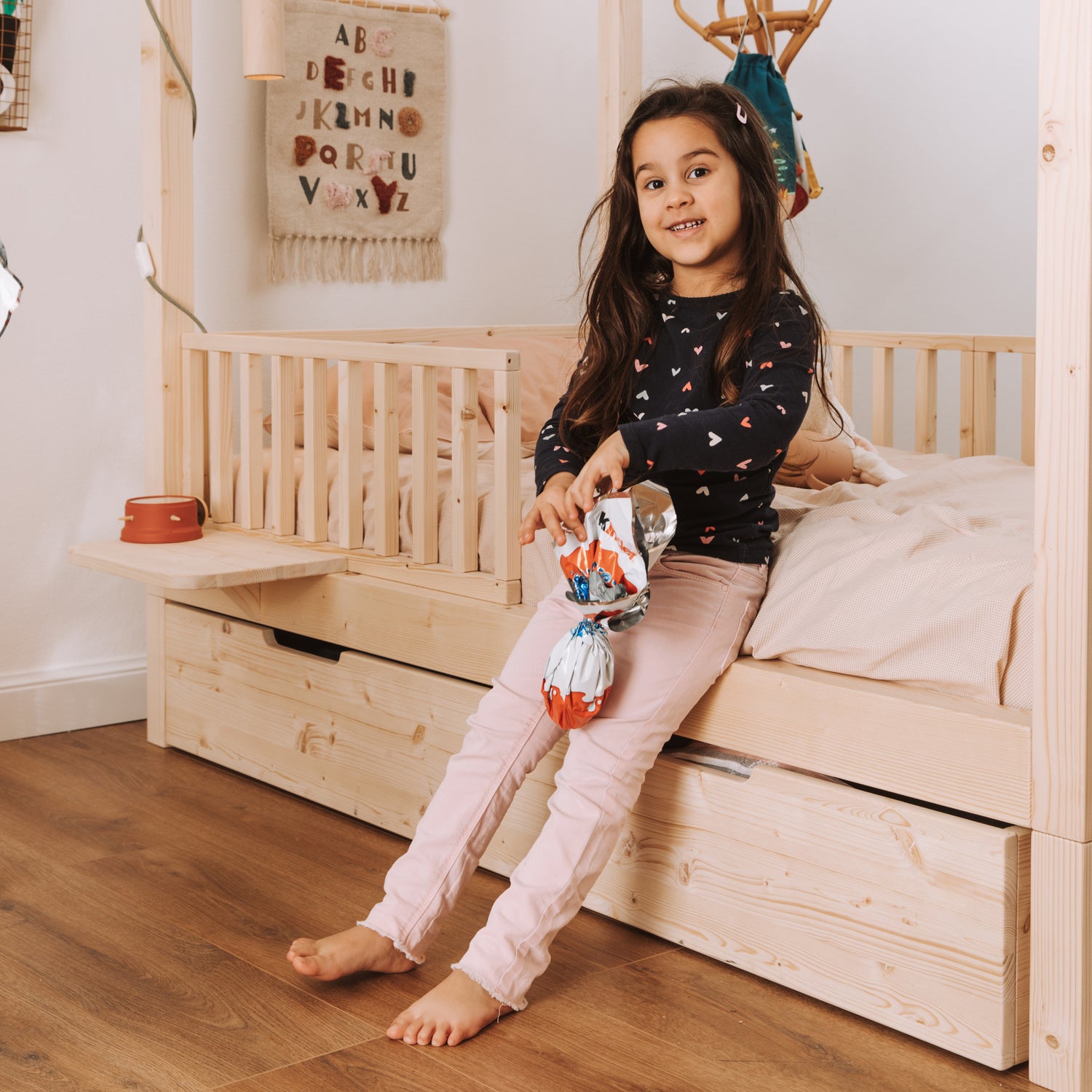 bambina vicino a lettino montessoriano con baldacchino e cassettone in legno naturale 
