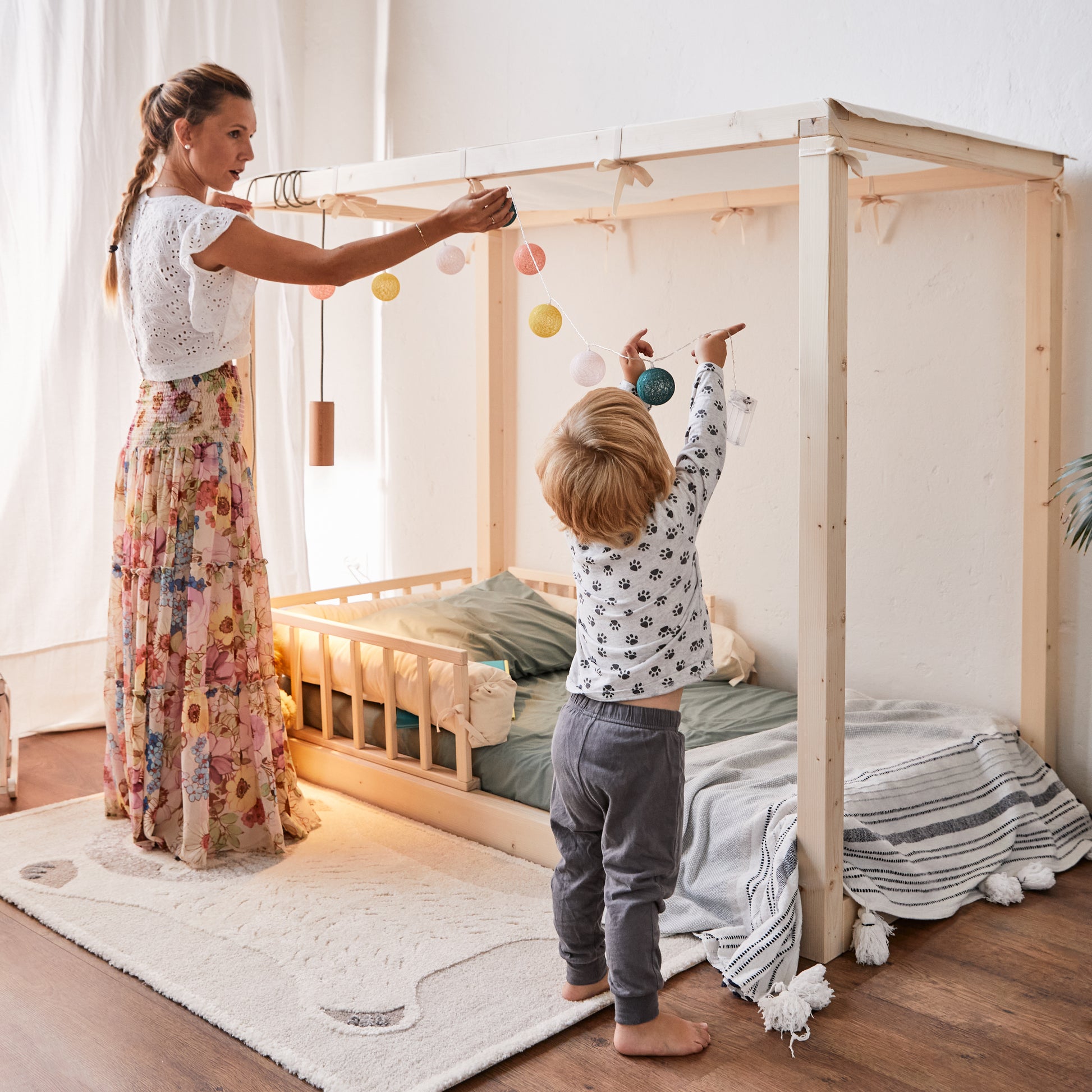Mamma e bambino decorano struttura in legno del lettino montessoriano nabè